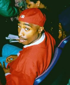 a young man sitting in a chair wearing a red hat and looking at the camera