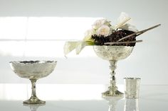 two silver goblets with flowers in them sitting on a table next to one another