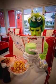 a woman with green hair sitting in front of a plate of fries and drink at a restaurant