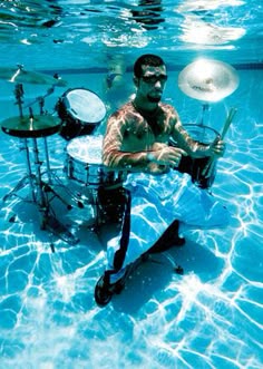 a man playing drums in the water with his feet up and head down under the water