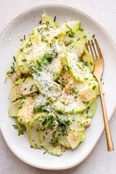 a white plate topped with zucchini and parmesan cheese next to a fork