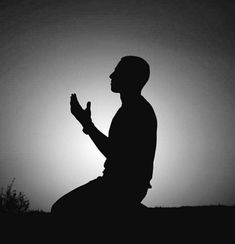 the silhouette of a man kneeling in front of the sun with his hands clasped to each other