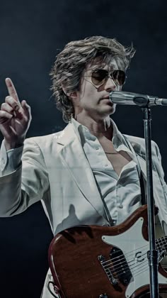 a man in white jacket and sunglasses holding up a guitar while standing next to a microphone