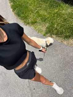 a woman holding a small dog in her hand while walking down the street with grass behind her