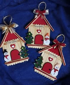 three small wooden houses with snowmen and christmas trees on them, hanging from bows