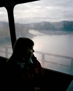 a woman sitting in front of a window next to a lake