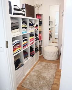 a white closet filled with lots of different types of clothes and rugs on top of hard wood flooring
