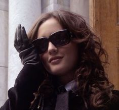 a woman in black jacket and sunglasses holding her hand up to her face