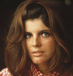 a close up of a person with long hair and blue eyes wearing a checkered shirt