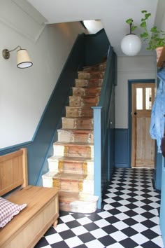 a hallway with stairs and checkered flooring next to a blue painted wall, potted plant in the corner