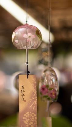 three glass ornaments hanging from strings with chinese writing on them and flowers in the background