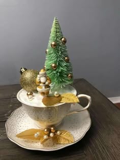 a christmas tree sitting in a teacup on top of a saucer with gold ornaments