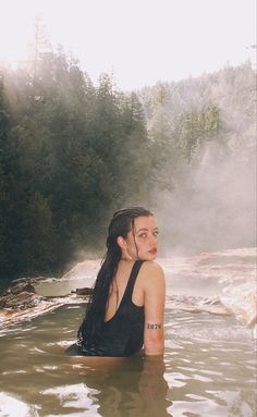 a woman sitting in the middle of a body of water with steam rising from her back