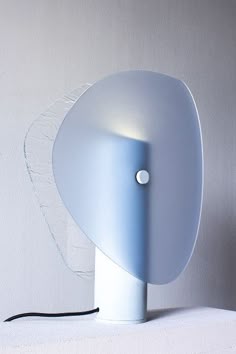 a blue lamp sitting on top of a table next to a white wall with a black cord