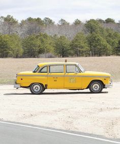 a yellow taxi cab is parked on the side of the road with trees in the background