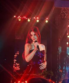a woman standing on stage holding a microphone in front of an audience at a concert