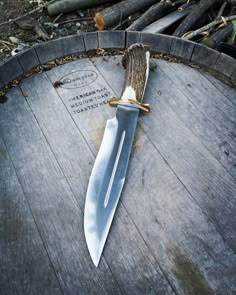 a large knife laying on top of a wooden table next to a tree stump and plaque