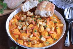 a white bowl filled with food on top of a wooden table next to silverware
