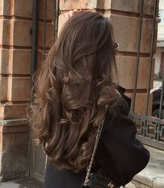the back of a woman's head with long, wavy hair and purse on her shoulder
