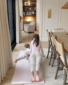 a woman sitting on top of a pink mat next to a child in white pants