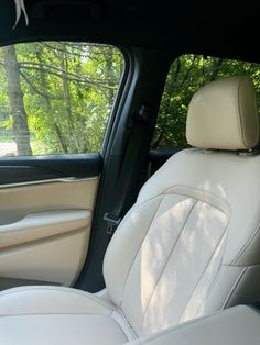 the interior of a car with white leather seats and trees in the back seat area
