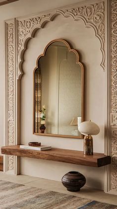 a large mirror sitting on top of a wooden shelf next to a wall mounted lamp