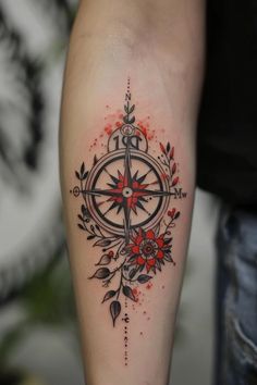a compass tattoo on the arm with red flowers and leaves around it's center