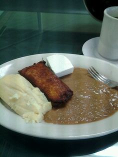 a white plate topped with mashed potatoes and meat next to a cup of coffee