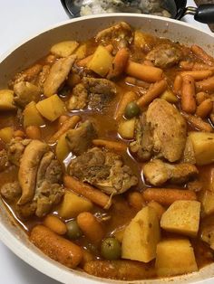 a white bowl filled with stew and carrots on top of a table next to a pot