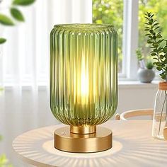 a green glass lamp sitting on top of a white table next to a potted plant