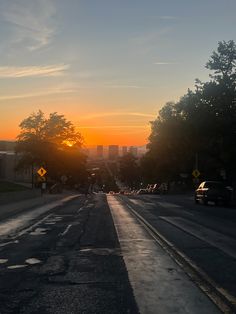 the sun is setting over a city street with cars parked on both sides and buildings in the background