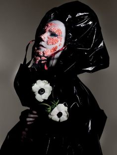 a man in a black plastic jacket with flowers on his face and blood dripping from his mouth