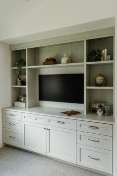 a large flat screen tv sitting on top of a white entertainment center next to cabinets