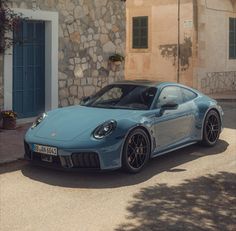 a blue sports car parked in front of a stone building with shutters on the windows