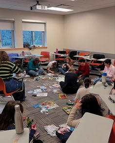 a group of people sitting on the floor in front of desks with papers all over them