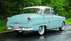an old blue car is parked on the side of the road in front of some trees