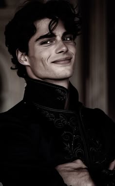 a man with his arms crossed smiling at the camera while wearing a black coat and tie