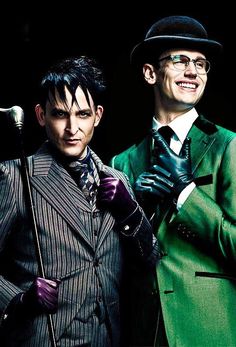 two men dressed in suits and hats standing next to each other with city lights behind them