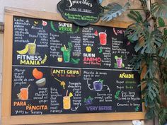 a menu board with different types of drinks on it and some plants in the background