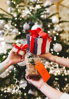two hands holding presents in front of a christmas tree with lights on the trees behind them