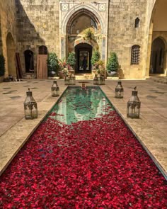an outdoor pool with red flowers on the ground and lanterns around it in front of a building