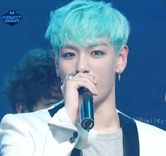 a male singer with blue hair holding a microphone in his hand and wearing a white jacket