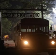 a school bus driving down the road at night with its headlights on and people walking by