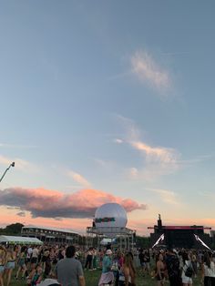 a crowd of people standing on top of a lush green field under a pink sky
