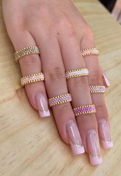 a woman's hand with five different rings on her fingers and one is wearing a pink manicure