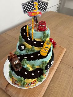 a three tiered birthday cake decorated with cars and trucks on a wooden table top