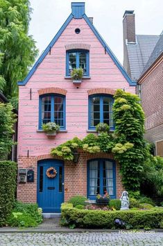 a pink house with blue shutters and green plants on the front door is surrounded by greenery