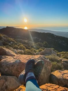 someone's feet resting on rocks overlooking the ocean and mountains at sunset or sunrise