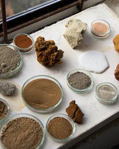 many different types of spices on a table next to a window sill with a rock in the middle