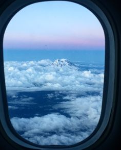 the view out an airplane window shows clouds and a snow capped mountain in the distance